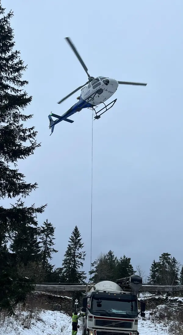 Helikopter løfter last over skog i vinterlandskap