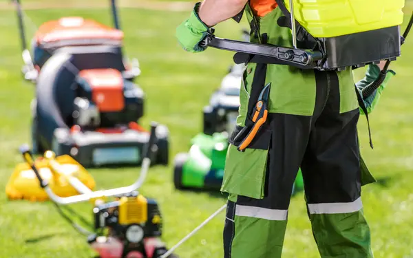 Vaktmester med gressklipper og vernebukse på plen